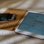 a tablet computer sitting on top of a bed next to a cell phone