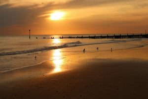 the sun is setting over the water at the beach